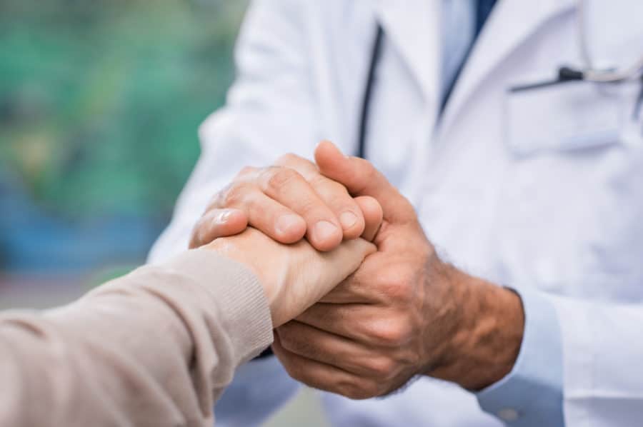 Close up of doctor hand reassuring her female patient at hospital. Closeup hands of medical doctor carefully holding patient's hands. Kind doctor giving real support for patient symbolizing care for those with chronic health conditions